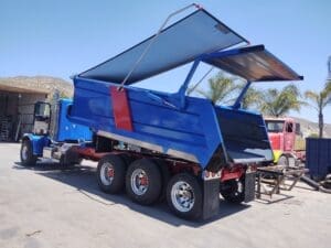 Blue dump truck with its hydraulic bed raised, ready to unload material in a desert lot.