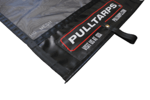 Close-up of a black tarp edge with a red-and-white 'PULL TARPS' label, showing mesh material and corner seam/grommet details.